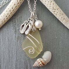 a sea glass necklace with shells and pearls hanging from it's side on a chain