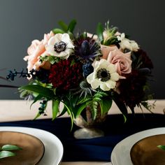 a vase filled with lots of flowers on top of a table next to two plates