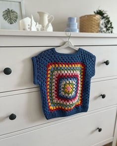 a blue crocheted sweater hanging on a white dresser next to a pot holder