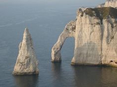 two large rock formations in the middle of water with cliffs on either side and one standing out into the distance