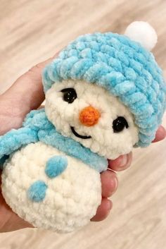 a hand holding a small crocheted snowman with a blue hat and scarf