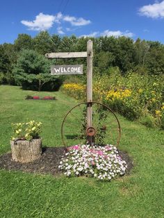 a welcome sign in the middle of a field with flowers around it and a wheel