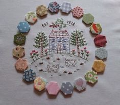 a white table cloth with various embroidered items on it and a house in the middle