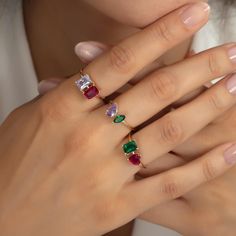 a woman's hand with three different colored stones on her fingers and two rings