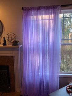 a living room with a fire place and a window covered in purple sheer curtaines