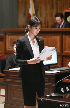 a woman standing in front of a desk holding papers