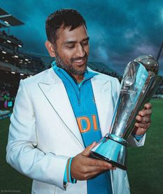 a man in a suit holding a trophy and looking down at his face while standing on a field