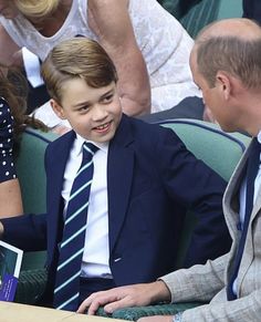 a young boy in a suit and tie sitting next to an older man at a tennis match