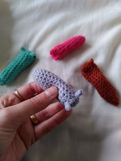 four crocheted toothbrush holders in different colors on a white sheet with a person's hand