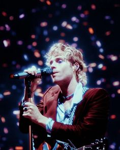 a man holding a microphone in his right hand and singing into the microphone on stage