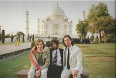 two men and a woman sitting on a bench in front of the taj mahal