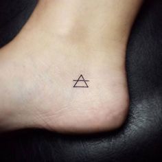 a small tattoo on the foot of a person with a triangle and an arrow in it