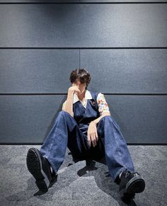 a man sitting on the ground with his head in his hands while wearing overalls