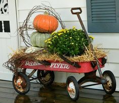 a red wagon filled with hay and pumpkins on top of a wooden floor next to a white house