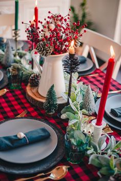 the table is set for christmas dinner with red and black plaid napkins, pine cones, evergreen greenery, silverware, and candlesticks