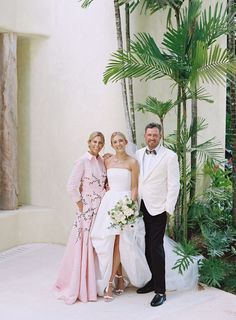 a man and two women standing next to each other in front of a palm tree