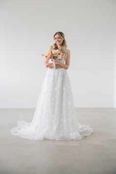 a woman in a white wedding dress holding an orange bouquet and posing for the camera