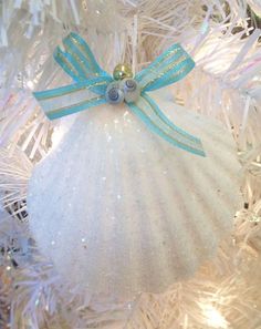 a white ornament hanging from a christmas tree with blue ribbon and bow on it