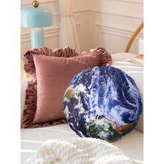 the earth pillow is on top of a bed next to a white blanket and blue lamp