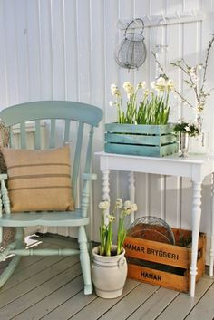 a wooden chair sitting on top of a porch next to a table filled with flowers