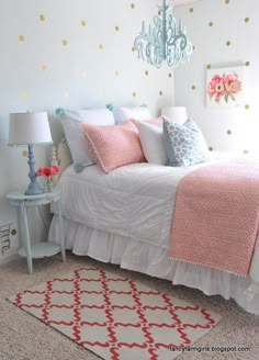 a white bed with pink and blue pillows in a bedroom next to a chandelier