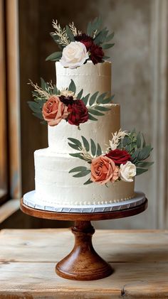 a three tiered cake with flowers and leaves on the top is sitting on a wooden stand