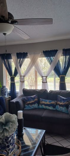 a living room filled with furniture and windows covered in blue drapes on top of them