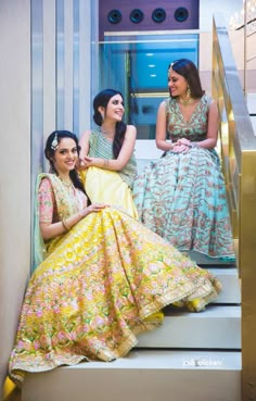 three women sitting on the steps in dresses smiling at each other and looking into the distance