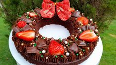 a chocolate cake decorated with strawberries on top of a white pedestal in the grass