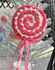 a pink and white lollipop with sprinkles on it sitting in front of a christmas tree