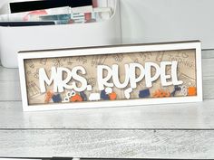 a sign that says mrs rupel on top of a wooden table next to a pen and pencil holder