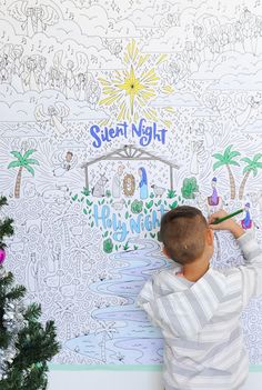 a young boy is drawing on the wall next to a christmas tree and a nativity scene