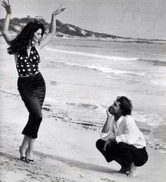 a man kneeling down next to a woman on a beach