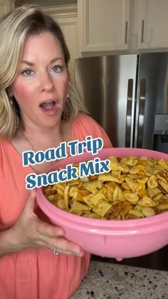 a woman holding up a pink bowl filled with food and the words road trip snack mix in front of her