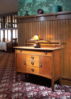 an old wooden desk with a lamp on it in a room that has wood paneling