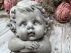 a statue of a baby laying on top of a wooden table next to pink roses