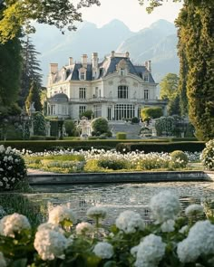 a large white house surrounded by greenery and flowers with mountains in the back ground