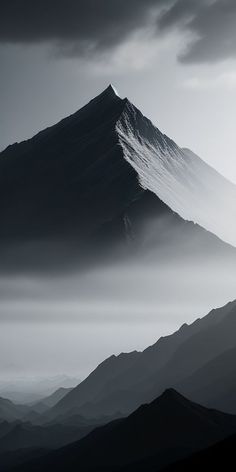 a black and white photo of a mountain in the foggy sky with low lying clouds