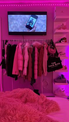 there is a television that is on in the room with clothes hanging up and a pink bed