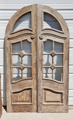 an old wooden double door with arched glass panels on the outside and inside, in front of a white building