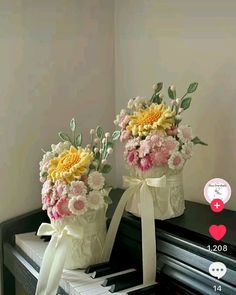 two vases filled with flowers sitting on top of a black piano keyboard next to each other