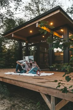 two people sitting on a wooden platform in front of a small cabin with glass walls