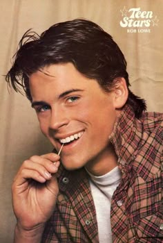 a young man smiling and holding a toothbrush in his mouth while wearing a plaid shirt