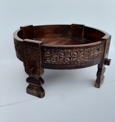 an old wooden bowl with carved designs on the sides and feet, sitting on a white surface