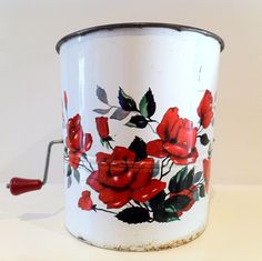 a white bucket with red roses painted on it and a metal handle that is attached to the side