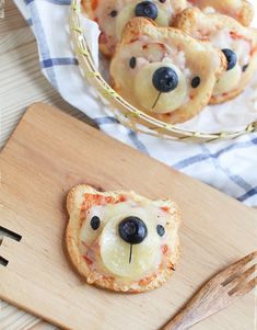 small pizzas with blueberries and cheese are on a wooden cutting board next to a basket