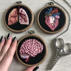 three embroidered brain images on black fabric, one with silver nail polish and the other with pink