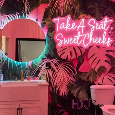 a bathroom decorated with neon lights and palm leaves on the wall, along with a pink toilet