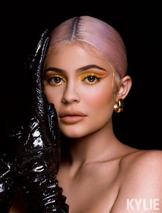 a woman with pink hair wearing black gloves and yellow eyeshadow, posing for the camera