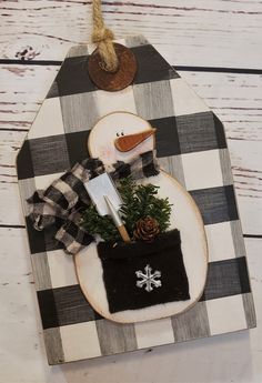 a snowman ornament is hanging on a white wooden board with black and white checkered fabric